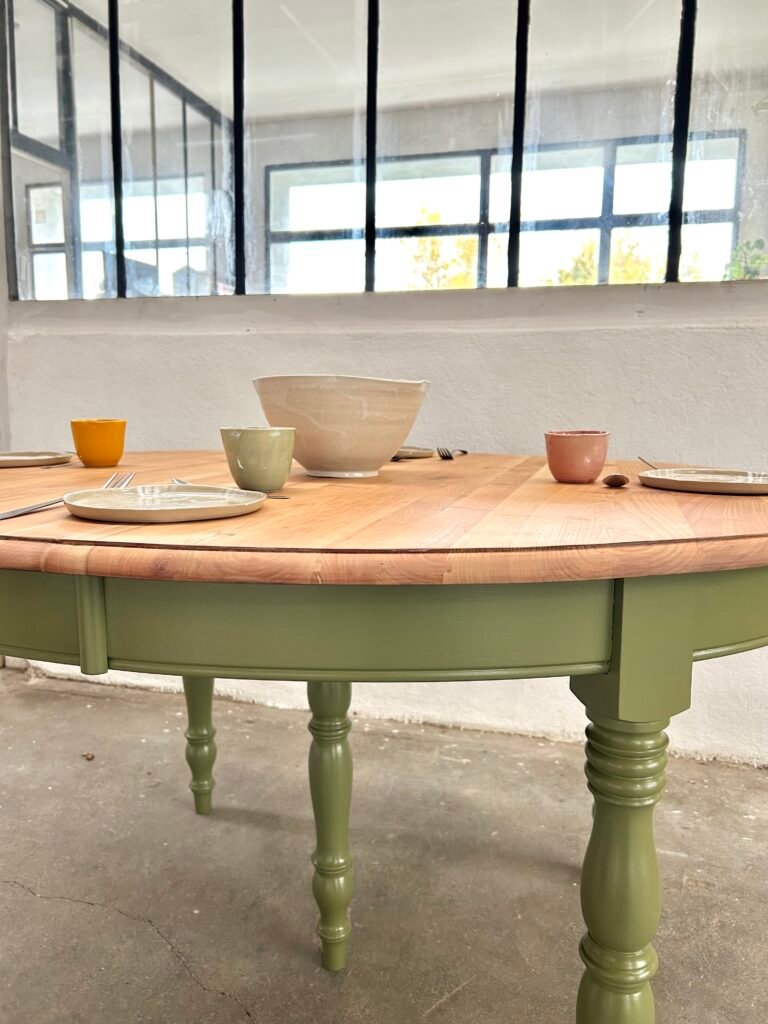 Une table de salle à manger en merisier, avec un plateau poncé et des pieds repeints en vert