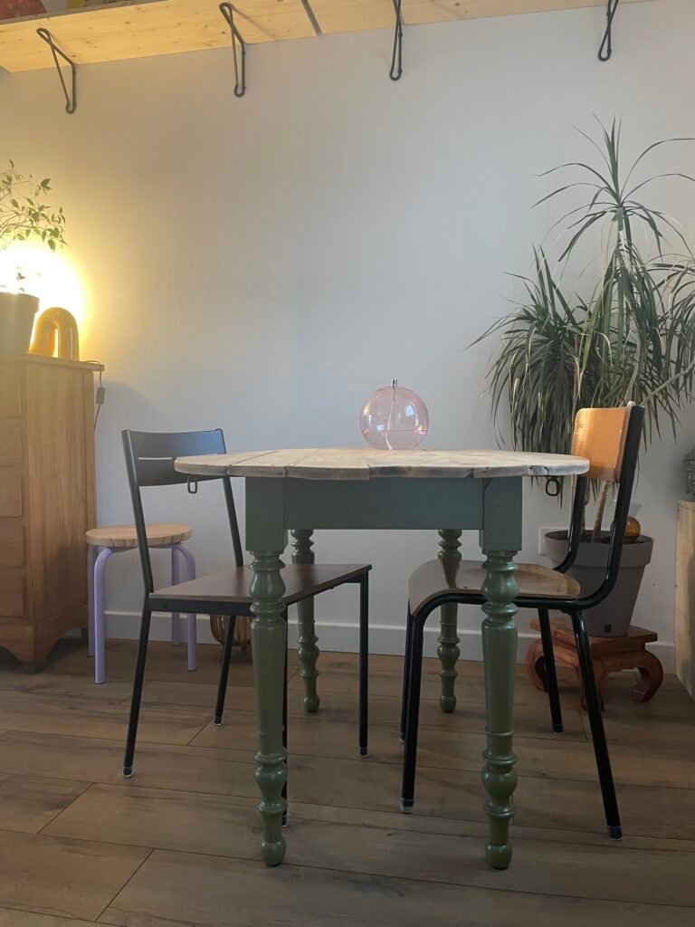 Une table ancienne rénovée avec un plateau poncé et des pieds peints en vert