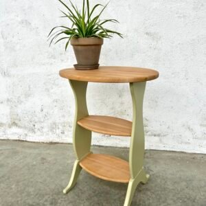 Un guéridon en merisier rénové avec un plateau et deux tablettes en bois clair et les pieds en vert tendre